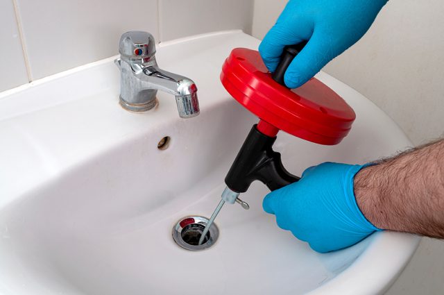 technician attempting to unclog clogged sink with drain snake